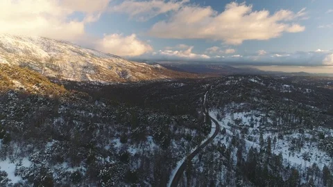 Aerial shot flying forward over winter forest, road below. Snowy hills. 库存影片 104236183