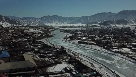 Aerial shot in forward movement of distant mountains and village with iced river 動画素材 165800887