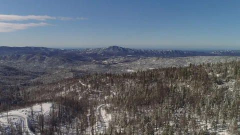 Aerial shot high over a forest in winter, with a road windying below. Video stock 103122291