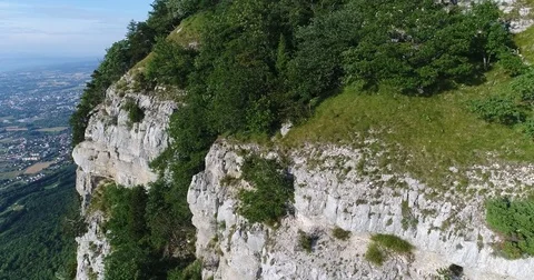 Aerial shot of limestone vertical cliff with trees, countryside below Stock-Footage 81380195