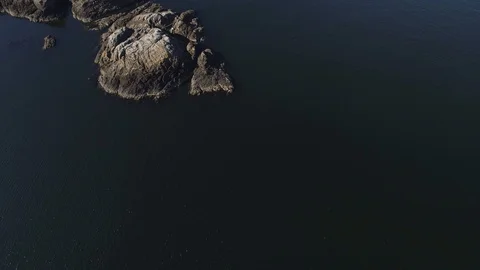 Aerial shot looking down and flying over rocks by ocean. Dark water. 库存影片 104671148