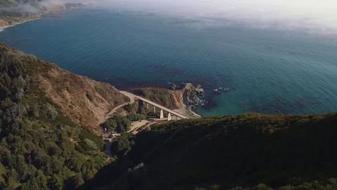 Aerial shot looking down at a bridge along rugged coast with blue water. Video stock 87562003