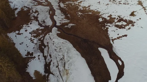 Aerial shot looking down, flying over meadow with patchy snow and creek. 库存影片 123895006