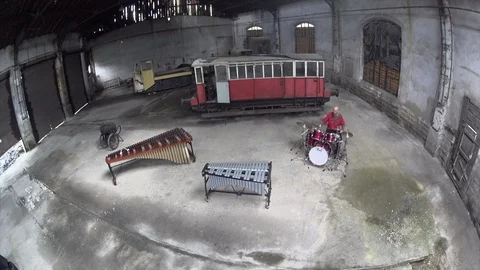 Aerial Shot of Man playing the drumset in red outfit - Old train repair factory, Stock Footage 104465441