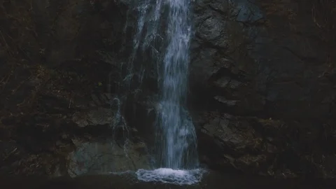 Aerial shot of man sitting in front of beautiful waterfall hidden in forest Stock Footage 87304076
