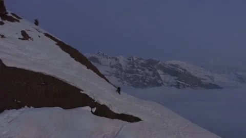 Aerial shot of a man walking alone in the snow and looking at the mountains Stock Footage 196892704