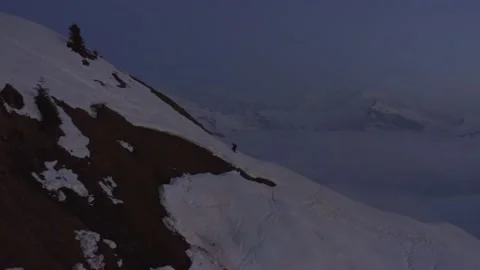 Aerial shot of a man walking alone in the snow to the top of the mountain Stock Footage 196893260
