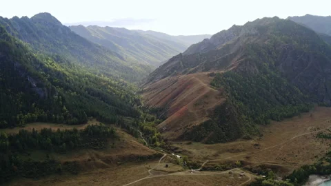 Aerial shot of mountain range, small river and several buildings at the foot Stock Footage 194379251