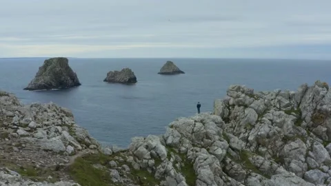 Aerial shot over a man facing the ocean surrounded by cliffs Stock Footage 195165159