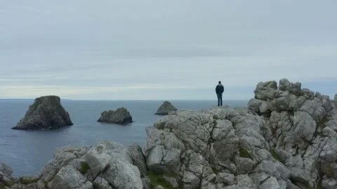 Aerial shot over a man facing the ocean surrounded by cliffs Stock Footage 195192924