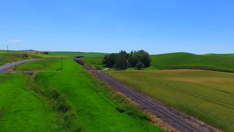 An aerial shot passing over a train that carries grain with a wheat field. Stock Footage 75024295