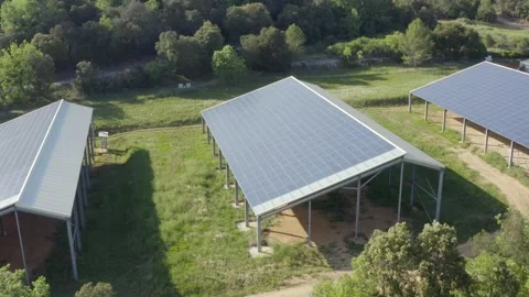 Aerial shot that revolves around a farm of photovoltaic panels on barn roofs Stock Footage 241163287