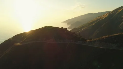 Aerial shot revolves around a hilltop overlooking the ocean with a windy road. 库存影片 87645358