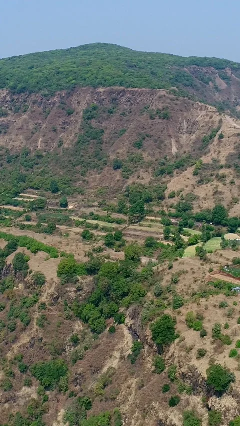 Aerial shot of rice fields on side of hill with steep rocky cliffs around Stock Footage 226875998