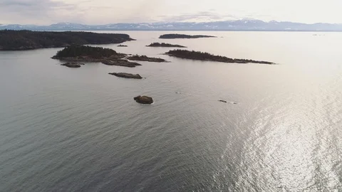 Aerial shot rising over sparse small rocky islands. Trees, sun glares on water. 库存影片 104772843