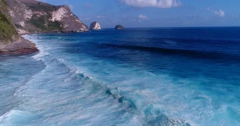 Aerial shot of rocky cliffs with waves breaking over shallow coral reef Stock Footage 99694969