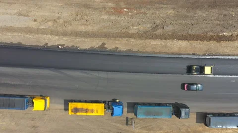 Aerial shot of roller making new asphalt road and trucks standing at roadside Stock Footage 326657632