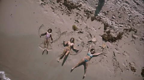 Aerial shot of three girls doing sand angels by ocean. Stock Footage 67488554