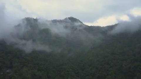Aerial shot through the clouds with a mountain behind, surrounded by forest Stock Footage 194472330