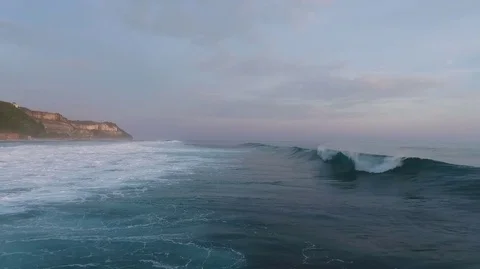 Aerial shot tracking with rolling surf and breaking waves, moving on shore along Stock Footage 78012185