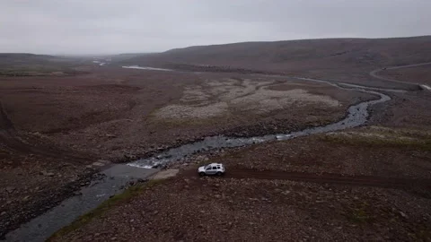Aerial shot tracking sideways a silver SUV driving through a stream in Iceland. 库存影片 165541266