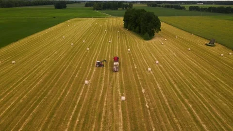 Aerial shot of a tractor working with a cargo truck and hay rolls in a 動画素材 251780615