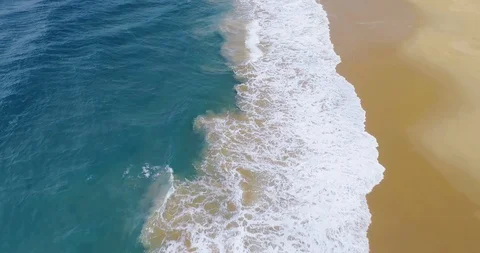 Aerial shot travelling over waves breaking on golden sandy beach Stock Footage 87573653