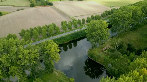 Aerial shot of van driving on tree lined road in agricultural area next to canal 動画素材 220038752