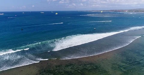 Aerial shot of waves breaking on reef with parasailing boats behind Video stock 79814917