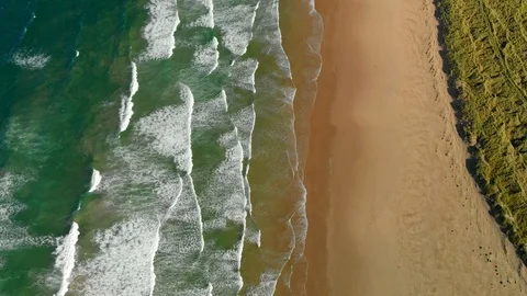 Aerial shot of waves moving  across green ocean towards beach and dunes Stock Footage 99072178