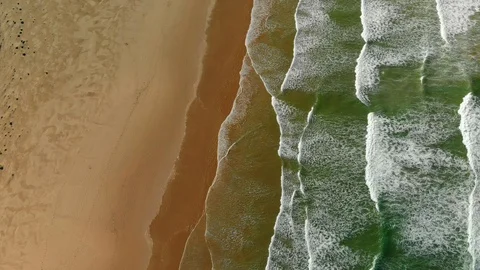 Aerial shot of waves moving  across green ocean towards beach and dunes Stock Footage
