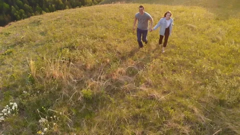 Aerial shot of a young couple happily running across a mountain meadow at sunset Stock Footage 111106653
