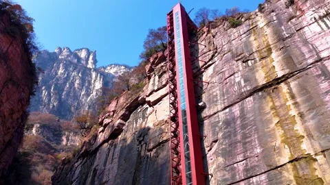 Aerial showcases a towering red elevator set against the dramatic cliffs of Stock Footage 297264444