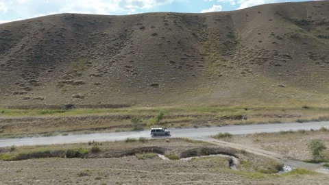 Aerial side view of a car on a valley road below dry hills, Kyrgyzstan Stock Footage 347241753