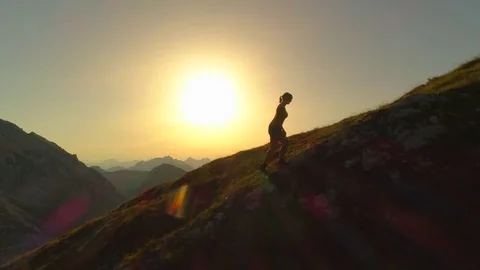 AERIAL SILHOUETTE: Woman trekker trying to reach mountain peak before sundown. Stock Footage