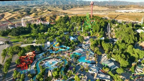 Aerial Six Flags Magic Mountain roller coaster and water rides, green trees  Stock Footage 244598162