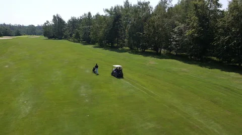 Aerial, slow motion- Golf player pushing his trolleys. Others driving in a buggy Stock Footage