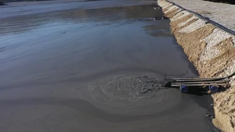Aerial slow motion view of mining residuals flowing into decanting pond Stock Footage 341925255
