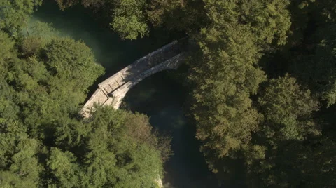AERIAL : Small amazing stone bridge above green river in lush overgrown forest Stock Footage
