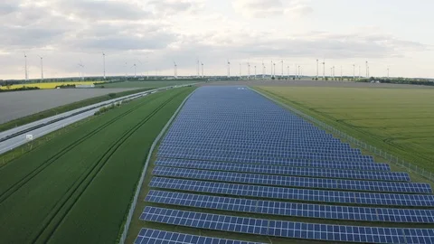 Aerial of solar panel field with road near and windmills in background, Germany Stock Footage