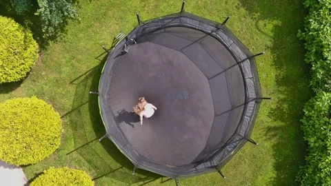 Aerial spinning top-down view of a girl jumping on a trampoline in a backyard 스톡 동영상 244654601