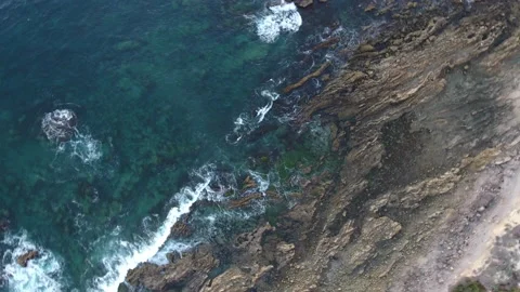 Aerial spiral pull away of dark blue waves rolling onto a rocky shore Stock Footage 157188300
