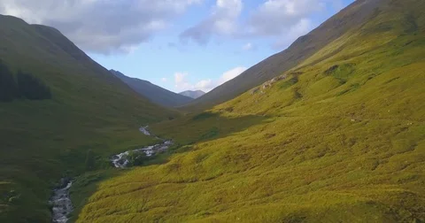 Aerial of stream of water flowing between lush green mountains on a sunny day Stock Footage 81534218