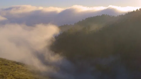 Aerial - Sun flare through clouds as they roll over mountains at sunrise Stock Footage 96529168