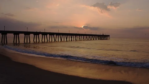 Aerial sun peeking behind clouds wide shot with pier Stock Footage