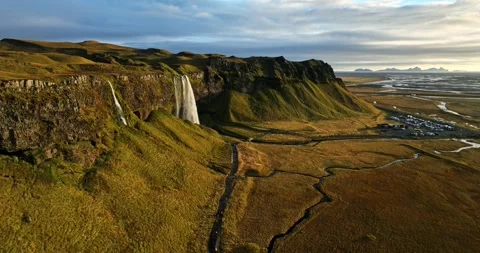 Aerial sunset view of a dramatic Iceland waterfall with golden cliffs, winding Stock Footage 334374190