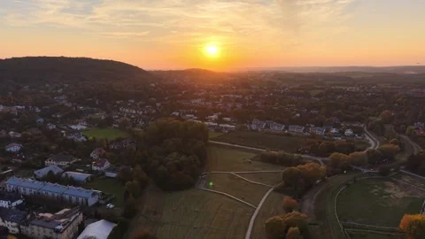 Aerial sunset view over suburban neighborhoods, wooded hills, open fields Видео 347384341