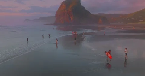 Aerial: Surfer leaving the ocean surf at sunset. Piha, New Zealand Stock Footage 247123721
