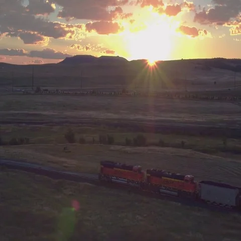 Aerial tacking daybreak sun pops out over Southern Colorado freight train Stock Footage 69454411