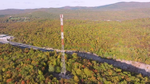 AERIAL: Telecom tower rising above colorful autumn woodland and asphalt highway Stock Footage 341368977